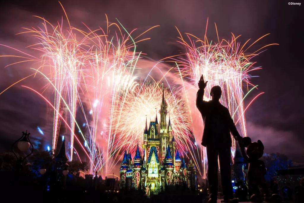 Cinderella Castle lit up with fireworks in the background and a statue of Walt and Mickey in the foreground