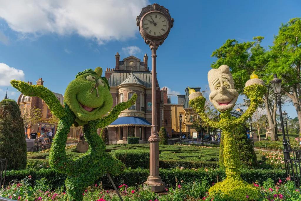 Topiaries shaped like Cogsworth and Lumiere from Beauty and the Beast in a flower bed