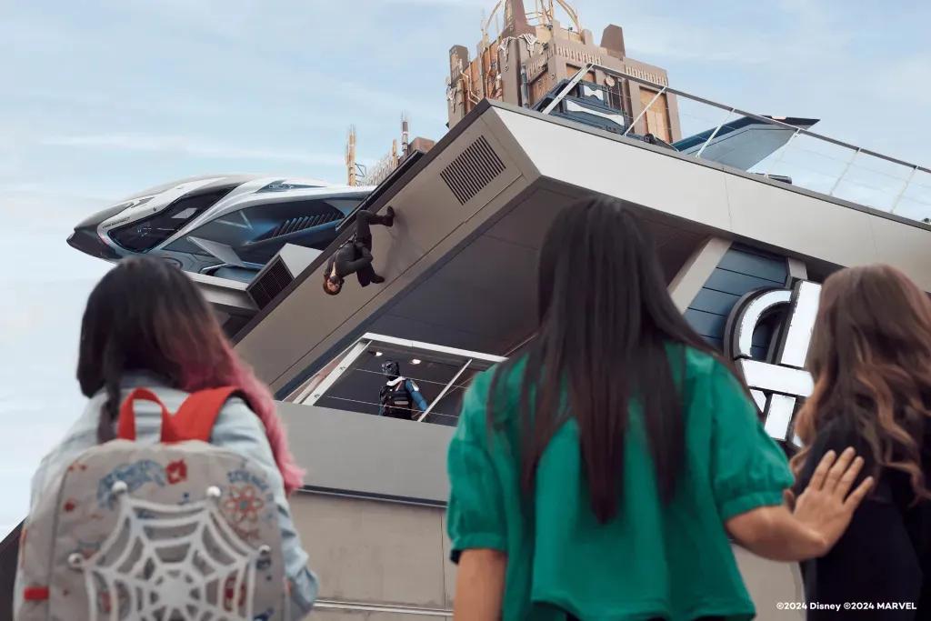 Drei Frauen schauen den Superhelden zu, die auf einem Gebäude des Avengers Campus klettern
