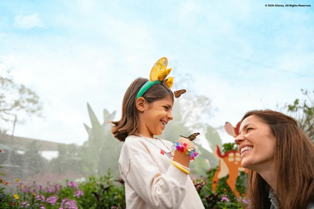 A woman laughing with a young girl who has had two butterflies land on her