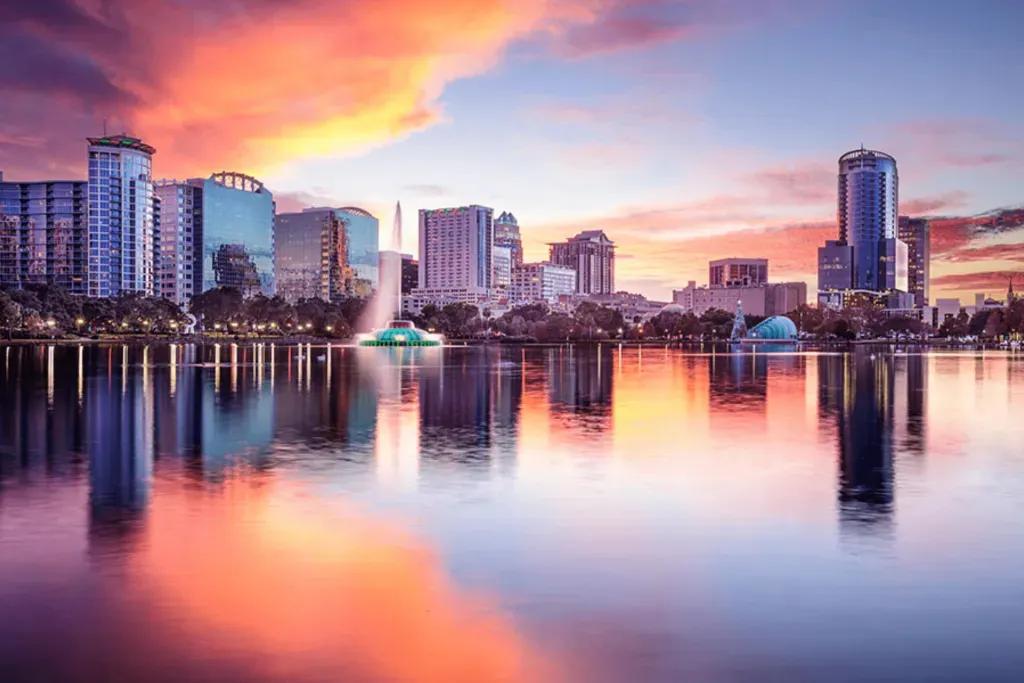 Lake Eola Park in Orlando zu Sonnenuntergang mit Spiegelung des orange, gelb und rosa gefärbten Himmels im Wasser des Sees