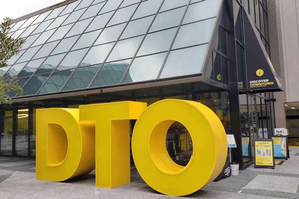 Glass building with a giant yellow DTO sign outside.