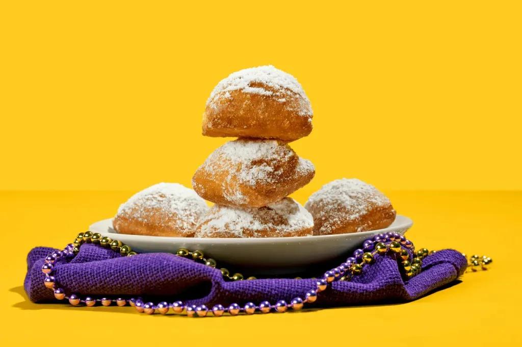  Ein Stapel Beignets auf einem Teller mit einer lila Serviette und Mardi Gras Perlen