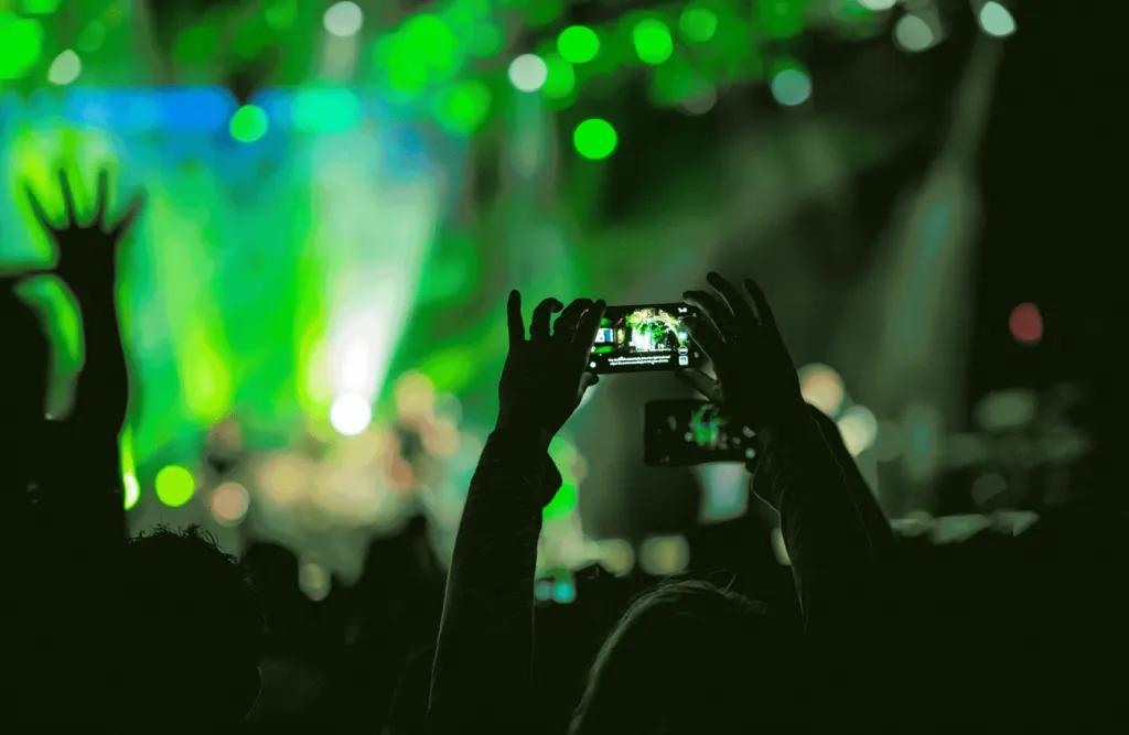 Someone in a crowd at a concert holding their phone above their head to take a picture of the stage