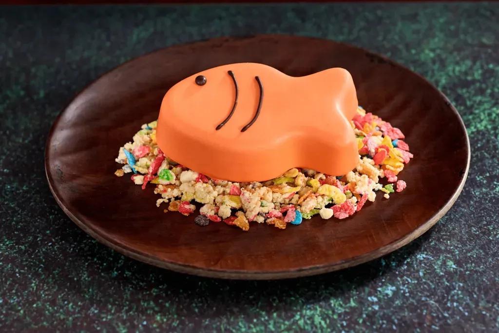 Ein orangefarbener Schokoladenmousse-Fisch mit braunen Details auf einem Reiskrispy-Müsliriegel.