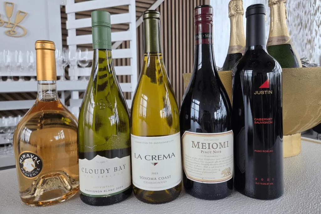 5 different bottles of wine lined up next to one another, with a couple of rose, a couple of white and a red wine.