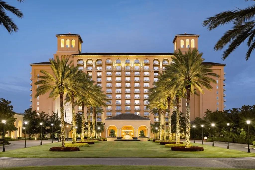 Large elegant building with a line of palm trees leading up to the lobby entrance.