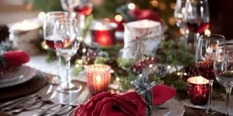 Christmas dinner table set with plates, crackers and Christmas tree lights in the background.