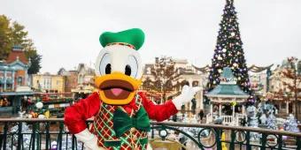 Donald Duck standing on a balcony pointing towards a large Christmas tree in the distance