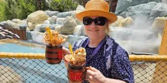 Woman in theme park holding two barrel themed mugs filled with drinks, whipped cream, sprinkles and more.