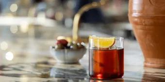 A clay vase next to a delicious drink on a bar top. The drink is a Negroni.