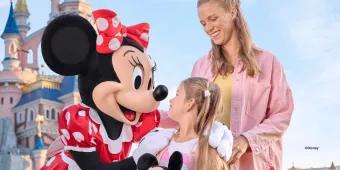 A young girl and her mother smiling with the Minnie Mouse character in front of Sleeping Beauty Castle at Disneyland Paris.