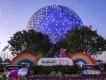 Spaceship Earth lit up in the early evening. In front of it is a large paint tube and a Festival of the Arts sign next to two rainbows