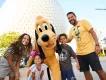A mother and father with a young boy and young girl posing with Pluto in front of Spaceship Earth