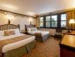 A forest/Bambi themed hotel room with two beds, a chair and a dresser