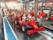 Small kids sat on rollercoaster car which is shaped like a red Ferrari Formula 1 car