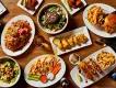 View from above a wooden table stacked with delicious dishes. From burger and chips, loaded nachos, pizza with cruditees and more!