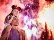 Young girl sat on her dads shoulders as the both look into the sky watching the magnificent fireworks above Cinderella Castle. There are many different colours and lights.