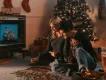 Couple sat playing with puzzle in front of a tv. Behind them there is a christmas tree and stockings hanging on the wall.