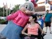 A young girl in an electric wheelchair looking up at a large bunny dressed in a pink jacket and pink bow.