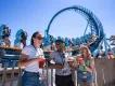 Three young adults stood in front of the Pipeline rollercoaster drinking cocktails and eating festival plates