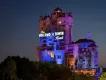 A large creepy looking tower standing tall above trees which looks like a run down, creepy hotel with a sign lit saying the Hollywood Tower Hotel.