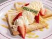 Zwei geviertelte Crêpes mit Schlagsahne, gelber Soße und Erdbeerscheiben.
