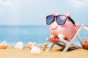 A pink piggy bank wearing sunglasses and sitting on a deck chair on a beach