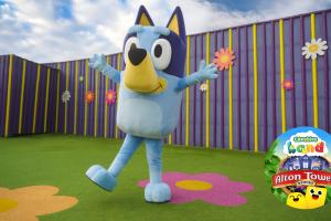 Big blue dog called Bluey with arms extended open and the Alton Towers CBeebies Land logo in the bottom right corner