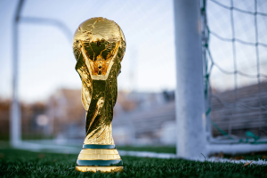 A gold trophy with a globe at the top and things wrapping around it sat in front of a white football goal.