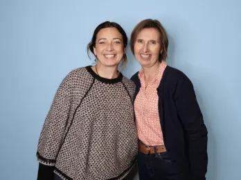 Two women smiling posing in front of a blue backdrop.