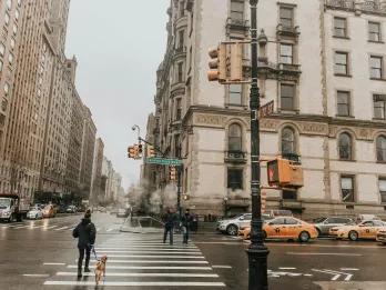 Beautiful cream buildings in NYC with roads outside covered in rain puddles and yellow taxis.
