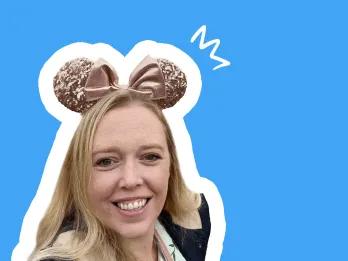 Smiling lady with long blonde hair, wearing pink mouse ears, blue background