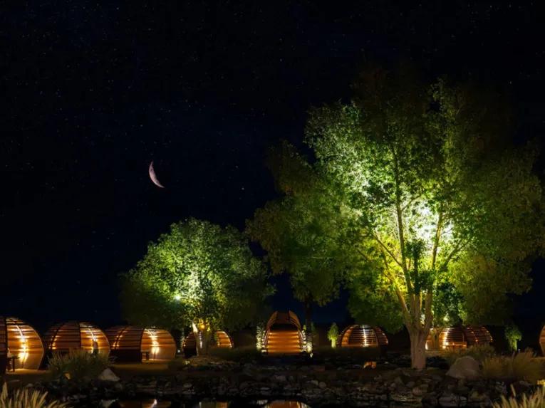 Luxury desert camp domes under a starry night sky with illuminated trees and crescent moon