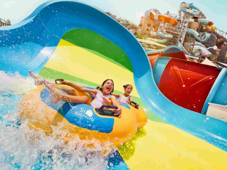 Two children having fun riding a shared inflatable tube at Yas Waterworld Abu Dhabi
