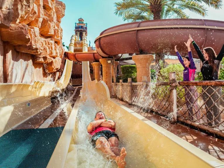 Person sliding down a water slide while others cheer at Wild Wadi Waterpark in Dubai